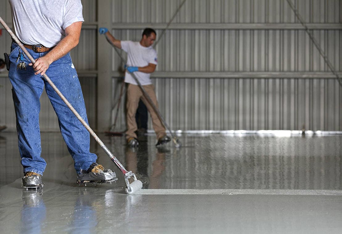 Worker applying epoxy floor coating inside a warehouse with a roller