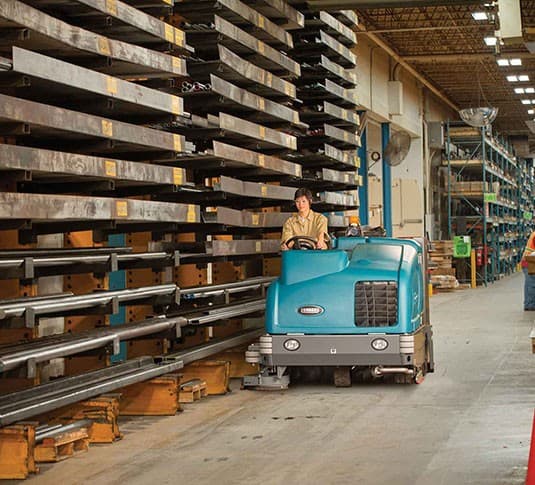 Ride-on industrial floor sweeper and scrubber in a warehouse
