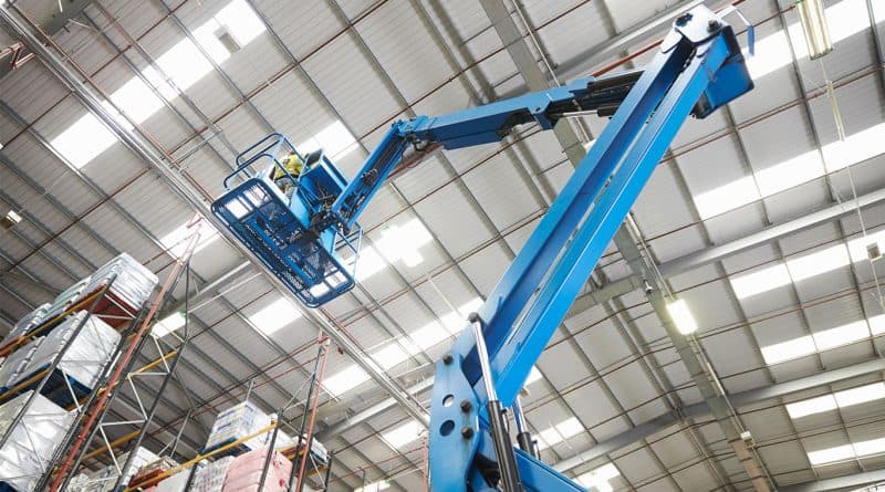 Worker applying industrial interior painting from a boom lift inside a warehouse