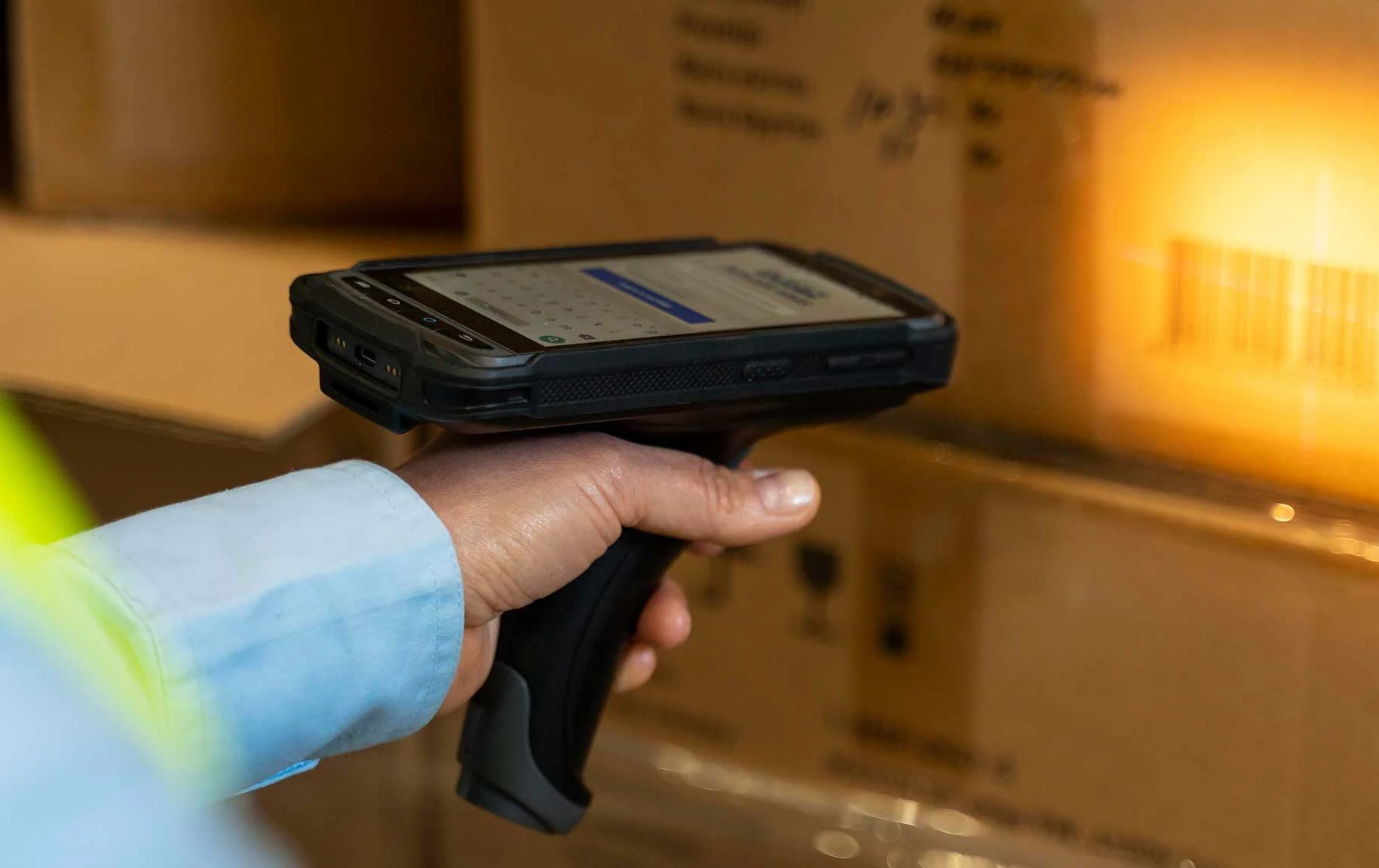Handheld barcode reader aimed at a labeled carton in a warehouse