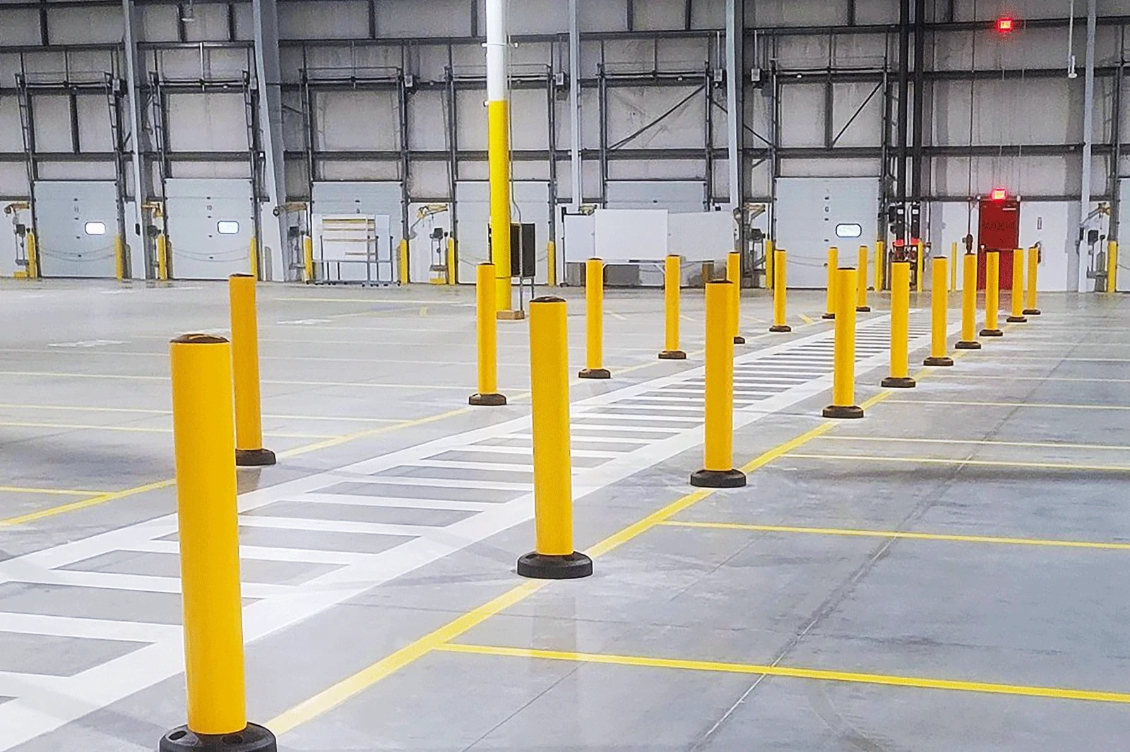 Defined pedestrian crossing and yellow protective bollards across an existing warehouse floor near loading docks