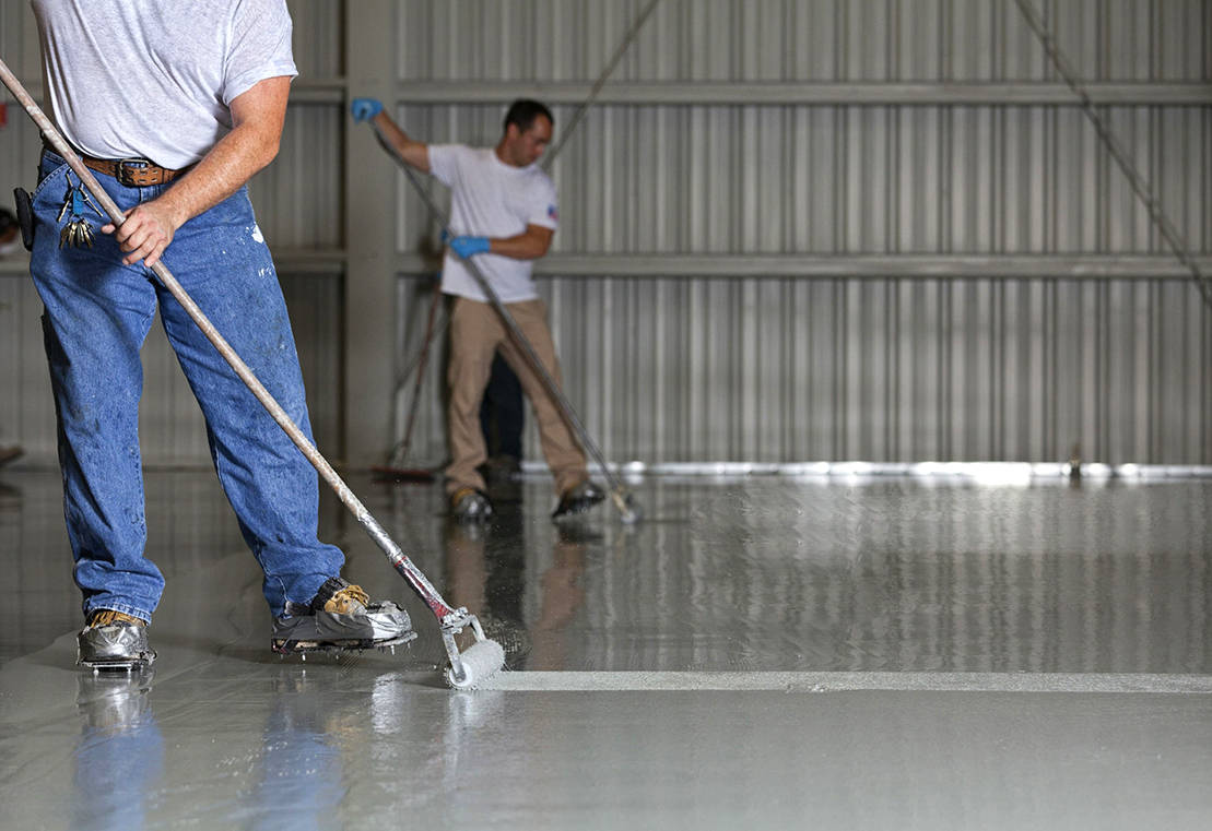 Worker applying epoxy floor coating inside a warehouse with a roller
