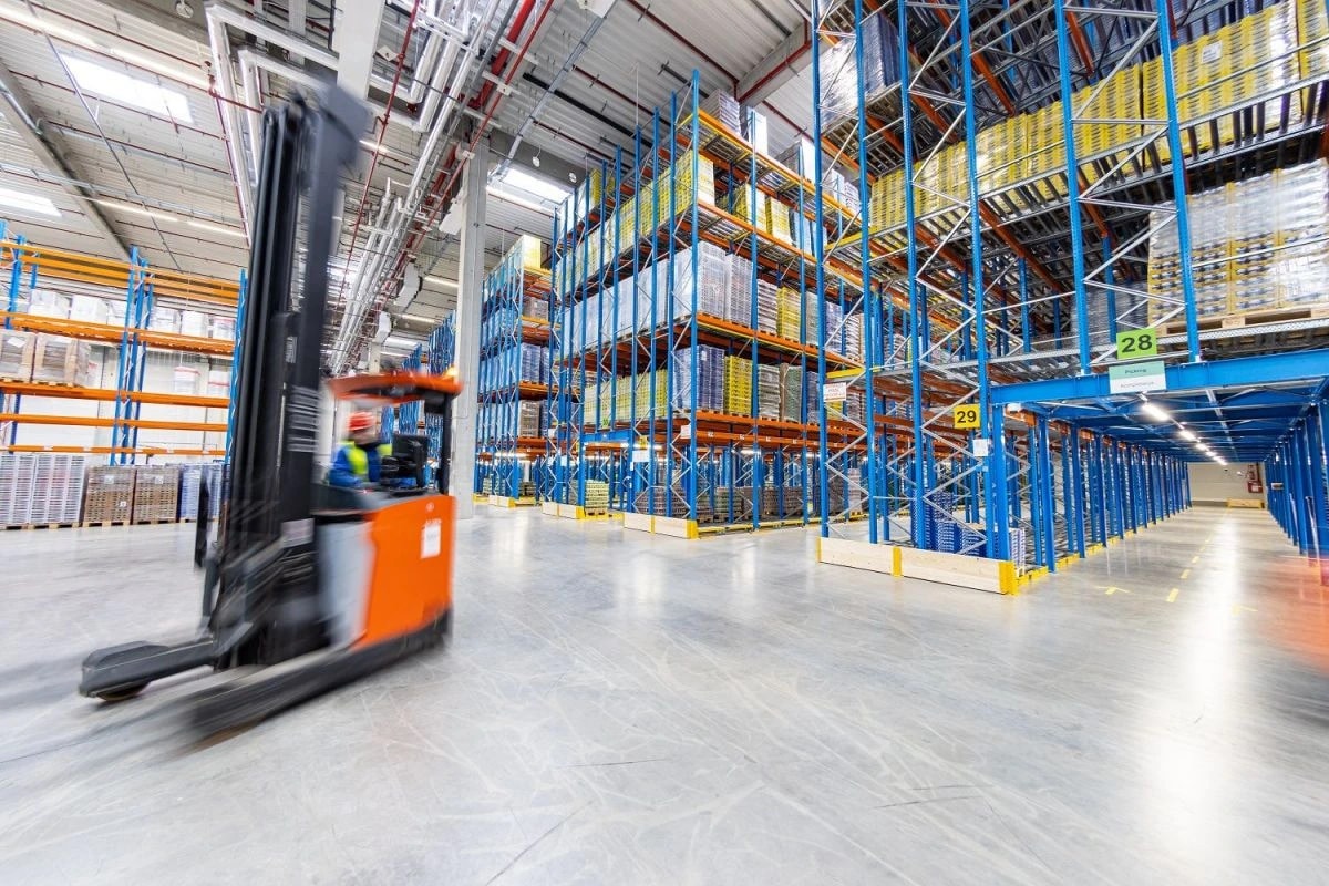 Wide warehouse interior with stocked blue and orange racks, protected routes and a reach truck