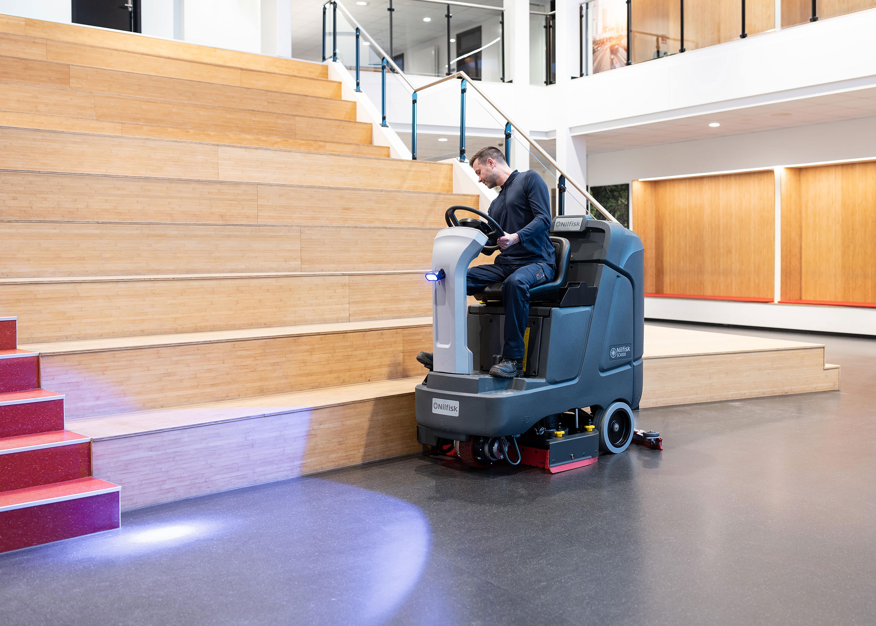 Operator using a ride-on floor scrubber in a large indoor facility