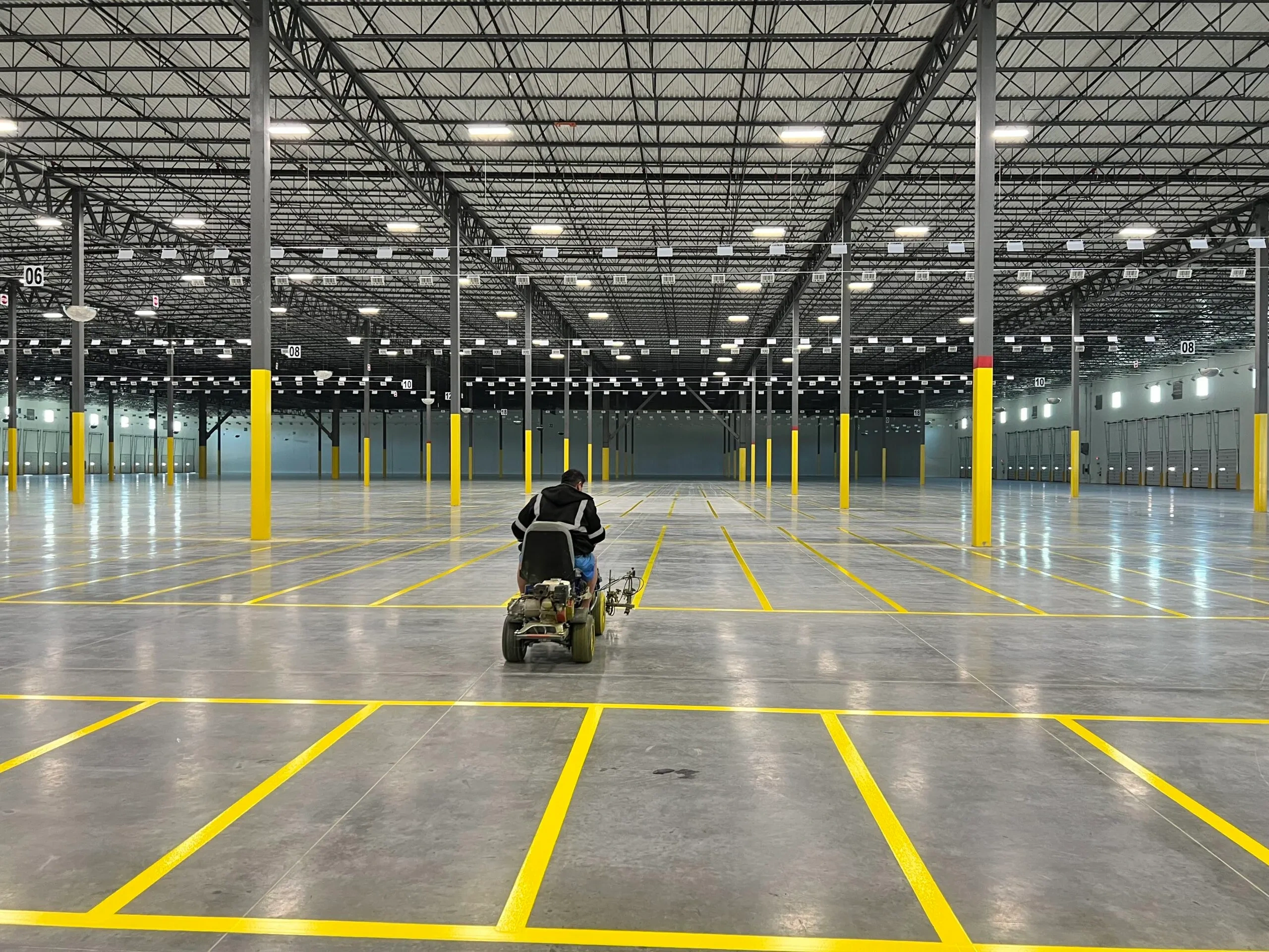 Operator applying yellow floor lines across a large warehouse