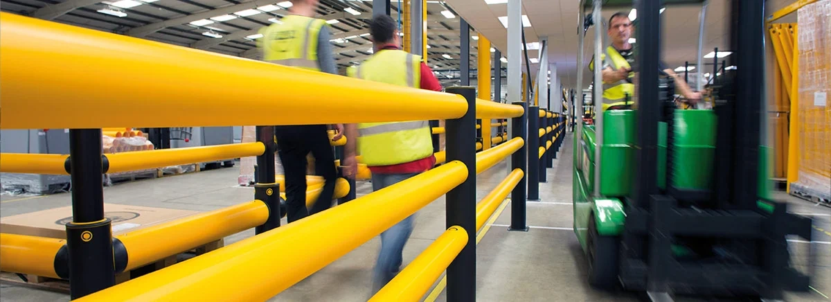 Yellow warehouse safety railing separating pedestrians from a forklift lane